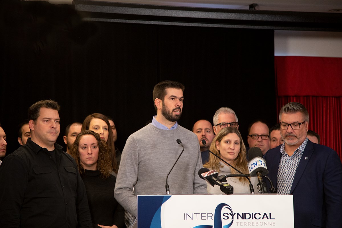 Au micro, Guillaume Tremblay, président du Syndicat des employés manuels de Terrebonne, avec à sa gauche Sylvain Roy, président du Syndicat des pompiers de la Rive-Nord et à sa droite, Chantal Riopel, présidente du Syndicat des cols blancs et Patrick Lepage, président de la Fraternité des policiers de Terrebonne, entourés de collègues et des membres des divers exécutifs syndicaux.