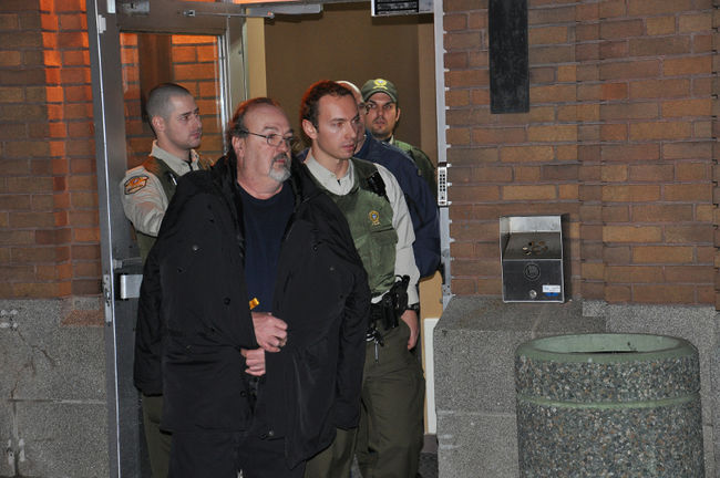 Gérald Genest est escorté à l'extérieur du poste de police de la Sûreté du Québec pour être transporté vers un centre de détention.