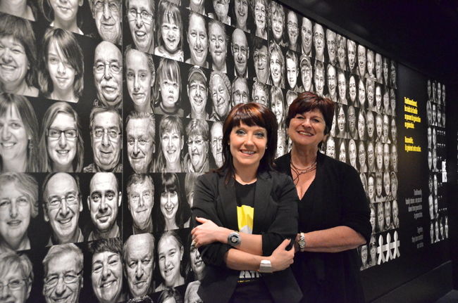La directrice de Boréalis, Valérie Bourgeois, et la présidente de la Corporation de développement culturel de Trois-Rivières, Stella Montreuil, posent devant la mosaïque de visages de la nouvelle exposition Générations.