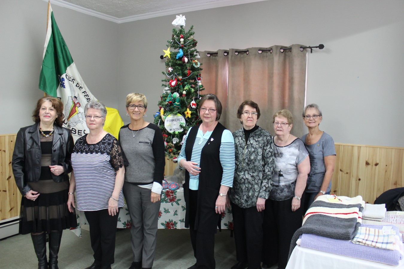 Les membres de l’exécutif accompagné de la mairesse Sylvie Bureau. Dans l’ordre habituel : Diane Ferland Dion, comité des communications et du recrutement; Jeannine Boucher, secrétariat et aide technique; Mme Bureau; Carmen Saint-Louis, présidente; Françoise Clément, comité des dossiers et de l’organisme OLO; Diane Martin, trésorière; Claire Larochelle, vice-présidente et comité des arts et textiles. À l’arrière, le sapin de Noël retenu par la Fédération 7 des Fermières.