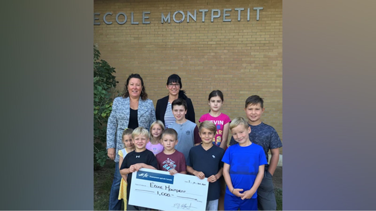 Lise Leclair de Financement agricole Canada (à gauche) en compagnie de Mélanie Gallant, directrice de l’École Montpetit de Saint-Crysostome (à droite) entourées d’élèves lors de la remise d’un chèque de 1 000 $ à l’école, pour son programme alimentaire scolaire.