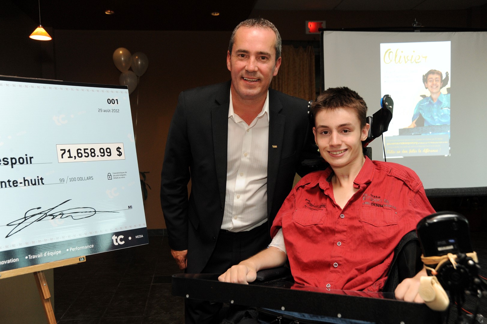 Olivier Gingras en compagnie de Serge Lemieux, vice-président Solutions Communautés locales Québec et Ontario lors d’un événement réunissant la famille Gingras, des représentants de la fondation et des employés ayant coordonné l’opération dans leur région respective.