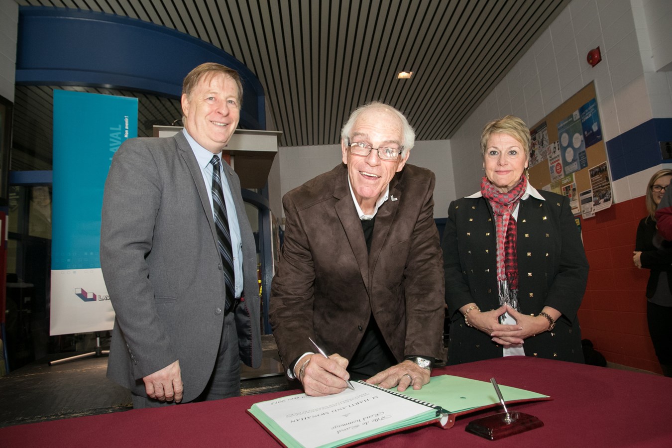 Hartland Monahan, entouré du maire de Laval Marc Demers et de son épouse Linda Geoffrion-Monahan, signe le Livre d'or de la Ville.