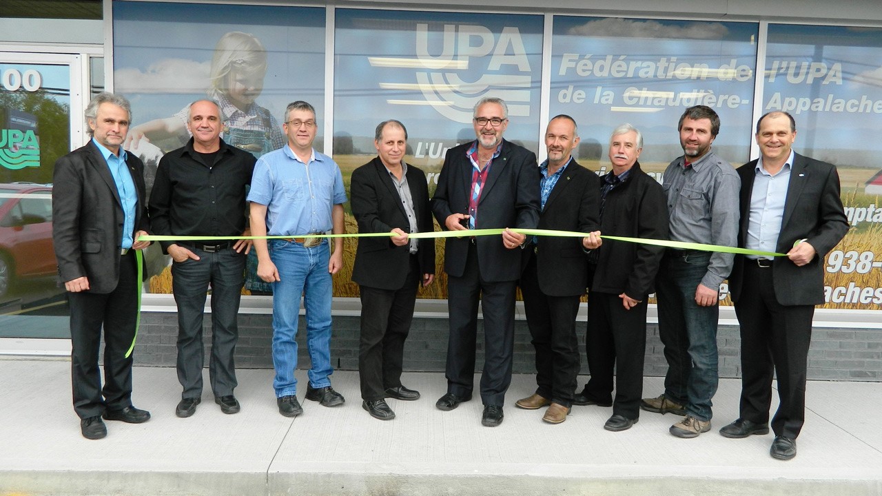 La photo regroupe les membres de l’exécutif de la Fédération ainsi que, complètement gauche, M. Roch Poulin, directeur régional, et complètement à droite, M. Marc-Ange Doyon, directeur adjoint. Au centre de la photo, tenant les ciseaux, M. Paul Doyon, président de la Fédération. Juste à sa droite (c’est-à-dire à votre gauche), M. Hervé Dancause, 1er vice-président, et à la gauche de M. Doyon (à votre droite), M. Jean Lambert, 2e vice-président.