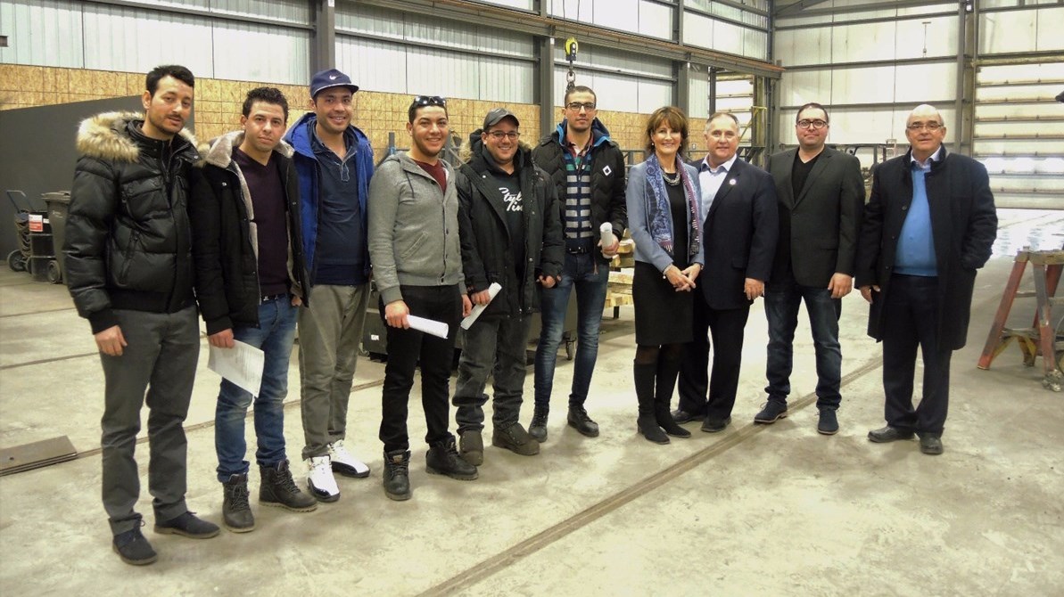 6 soudeurs provenant de la Tunisie qui travaillent actuellement chez Structure SBL à Saint-Benoît-Labre, accompagnés de Kathleen Weil, ministre de l'Immigration, de la Diversité et de l'Inclusion, Paul Busque, député de Beauce-Sud, Hugo Veilleux, directeur général et vice-président chez Structure SBL et Martin Binette, président chez Structure SBL. 