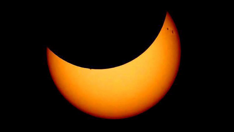 La partie orange représente le Soleil et la partie noire, la Lune. Les petites taches sombres sont quant à elles des taches solaires.