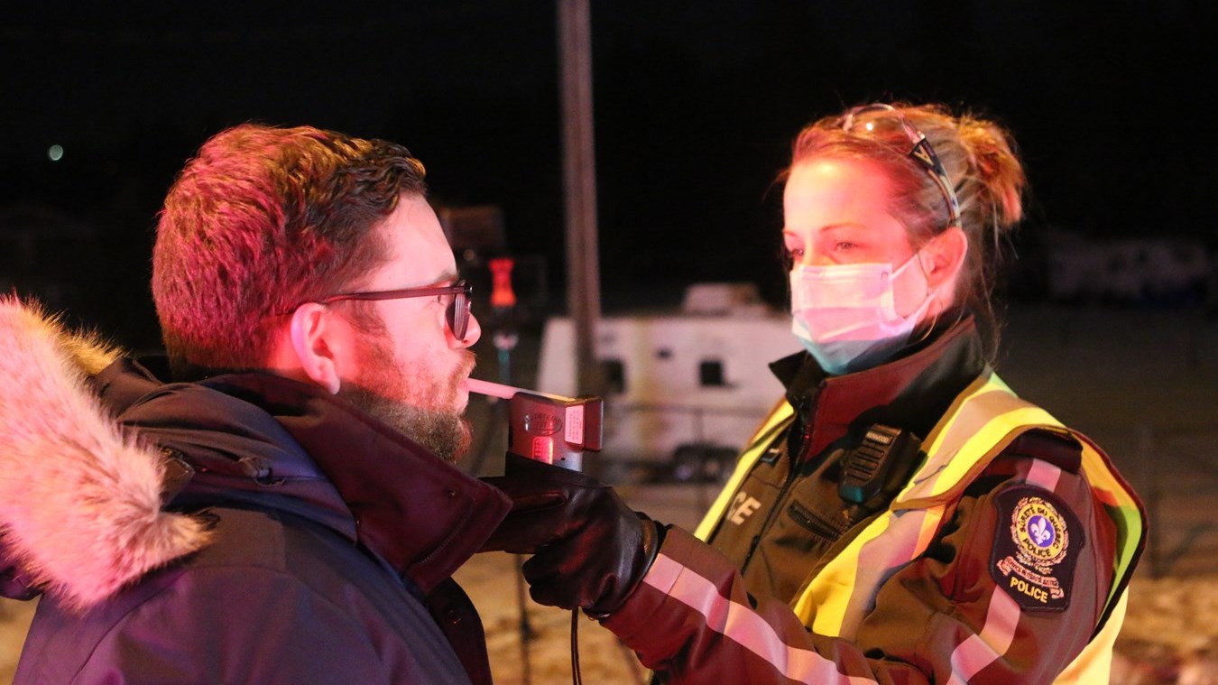 Une agente de la Sûreté du Québec faisant souffler un citoyen dans l'appareil de détection approuvé sur un barrage pour l'alcool au volant.