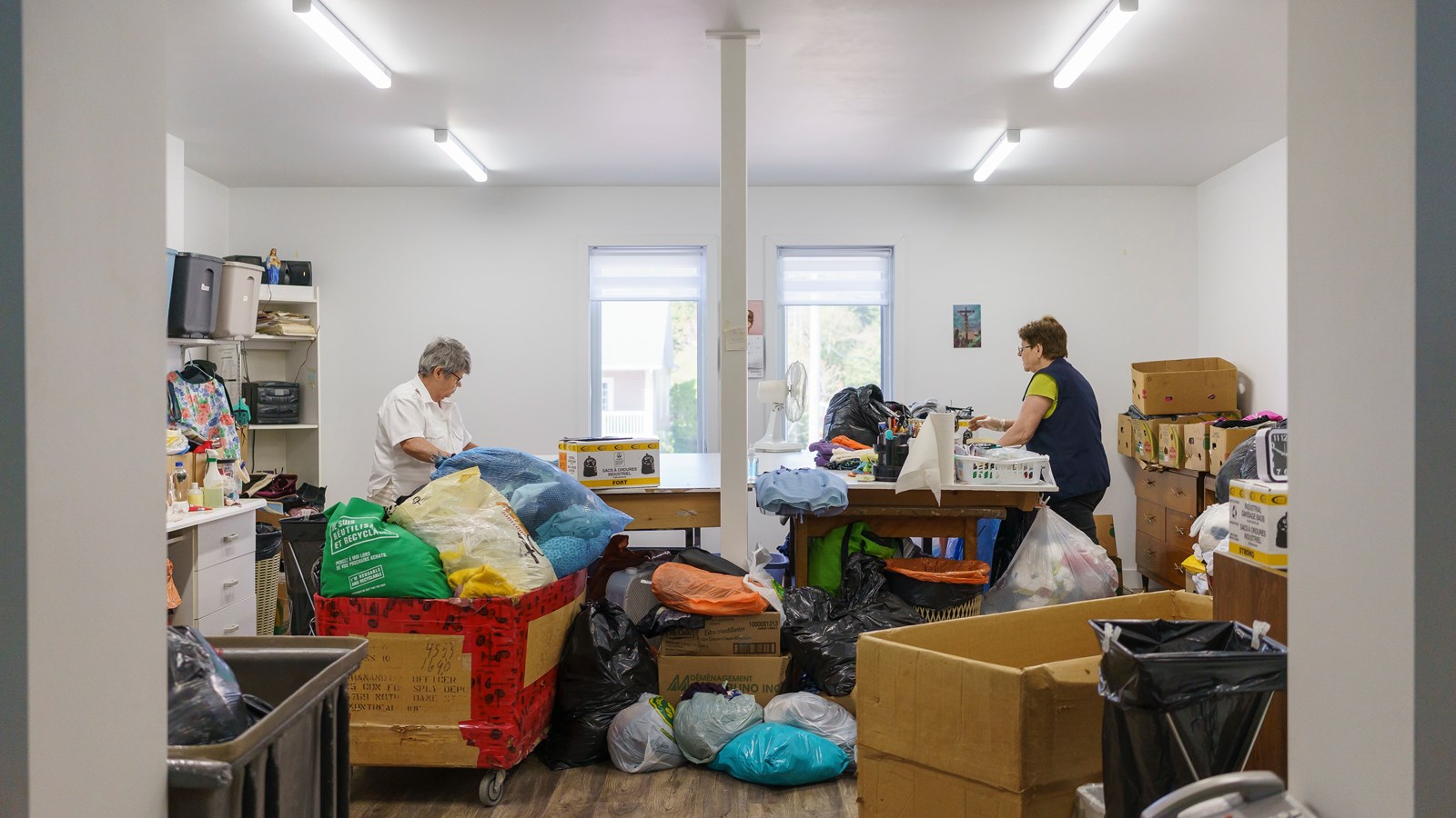 Ici, deux personnes séparent le linge d’adultes dans des bacs pour l’hiver ou pour l’été.