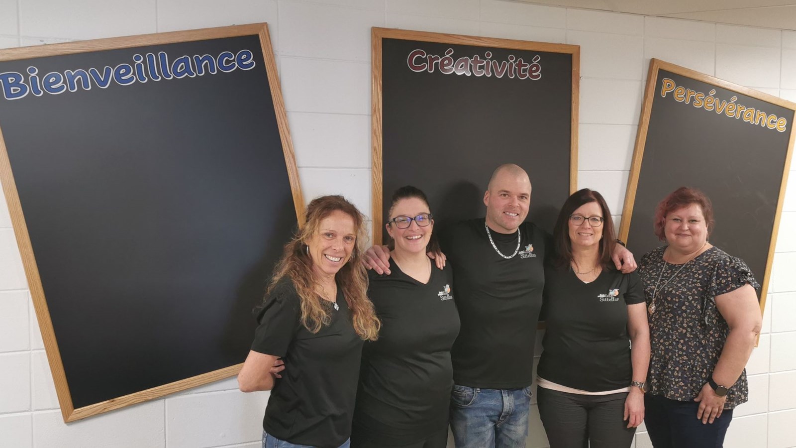 Julie Létourneau, éducatrice spécialisée, Marie-Ève Fortin, enseignante, Vincent Létourneau, directeur, Dany Fecteau, du service de garde et Jessica Déry, présidente du comité d'établissement, devant les tableaux des trois valeurs: bienveillance, créativité et persévérance.