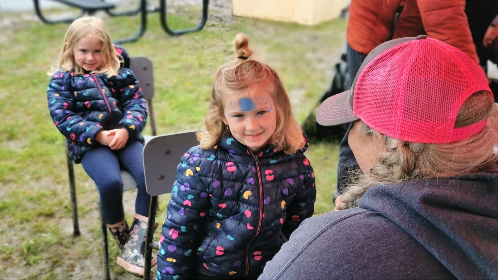 Estelle attend patiemment que le maquillage festif soit complété sur le visage de sa jumelle Sofia, pour avoir le même traitement. 